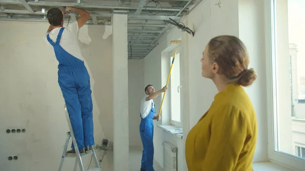 Женщина смотрит, как ремонтники работают в квартире — стоковое фото