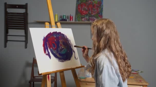Девушка рисует картину и смотрит на нее — стоковое видео