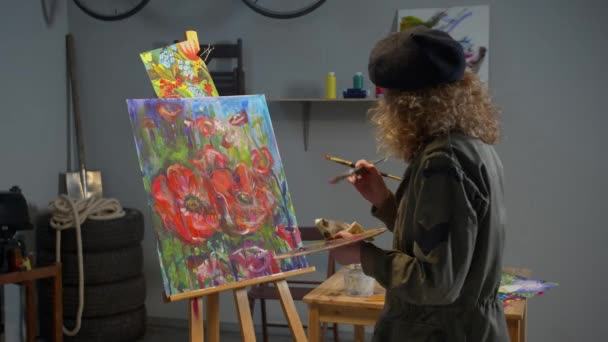 Женщина рисует цветы на холсте в студии — стоковое видео