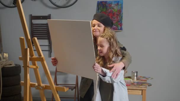 Chica pone lienzo en un caballete, mujer explica cómo dibujar — Vídeos de Stock