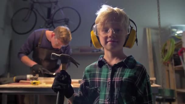 Jongen met bril staat met hamer en kijkt naar de camera — Stockvideo