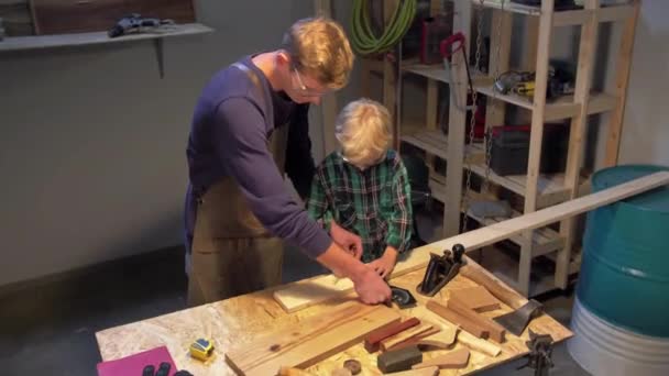 Чоловік показує хлопчикові, як виміряти дошку в майстерні — стокове відео