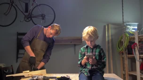 Ragazzo siede con il telefono, l'uomo lavora in un laboratorio — Video Stock