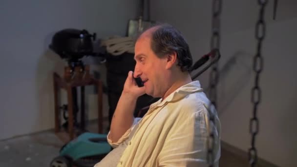 Чоловік сидить і розмовляє по телефону в майстерні — стокове відео