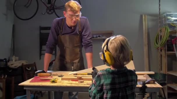 Ο άνθρωπος δείχνει ένα ξύλινο προϊόν σε ένα αγόρι σε ένα εργαστήριο — Αρχείο Βίντεο