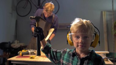 Gözlüklü çocuk elinde çekiçle kameraya bakıyor, ağır çekimde.