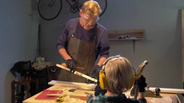 Adam tahtayla çalışıyor ve çocuk ona bakıyor. 