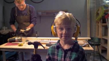 Gözlüklü çocuk elinde çekiçle kameraya bakıyor. 