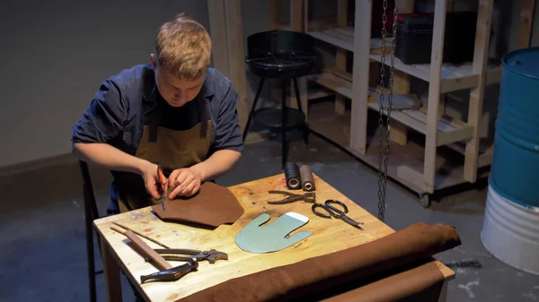Чоловік вирізає шматок тканини для взуття на столі — стокове фото
