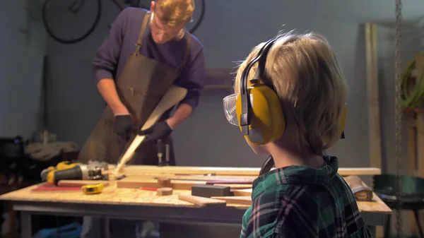 Jongen kijkt naar werkende man in de werkplaats — Stockfoto