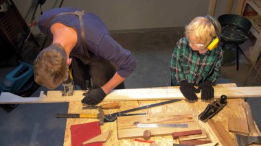 Ağır çekimde, çocuk atölyede önlüklü adama yardım eder.