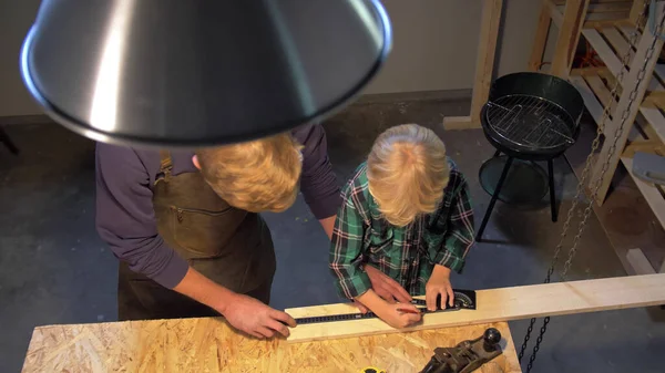 Homme et garçon travaillent avec une planche de bois dans l'atelier, au ralenti — Photo