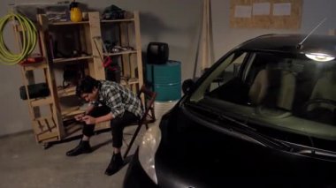 Adam garajda telefonla oynuyor.