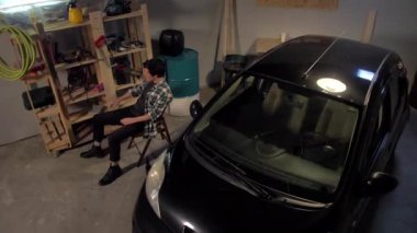 Adam garajda bira içip sigara içiyor.