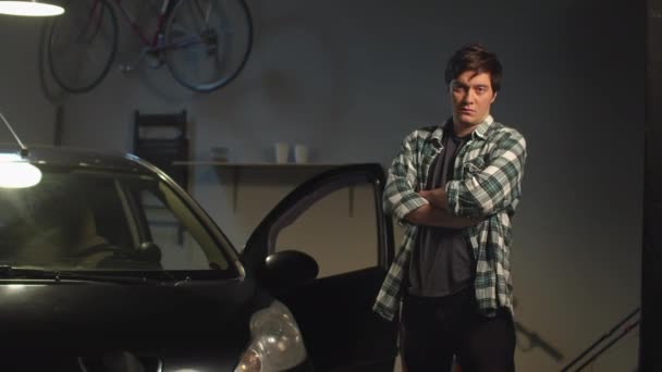 Un hombre posa cerca de su coche en un garaje. Vista panorámica — Vídeos de Stock