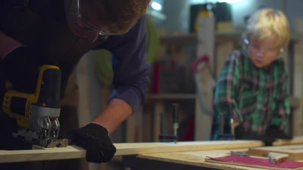 De jongen helpt pa om een plank te knippen. Schuiven — Stockvideo