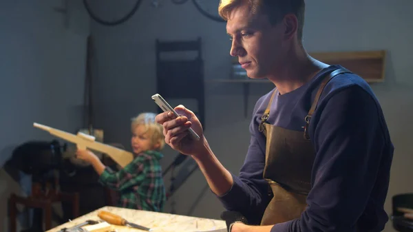 Мужчина пользуется мобильным телефоном, пока его ребенок играет в гараже — стоковое фото