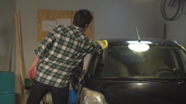 Sürücü arabasının ön camını bir bez parçasıyla siliyor.