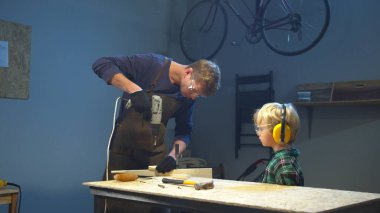 Çocuk babasının bir tahtayı delmesini izliyor. Orta uzunlukta.