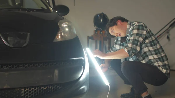 En mekaniker inspekterar en bil med en lampa och pratar i telefon — Stockfoto