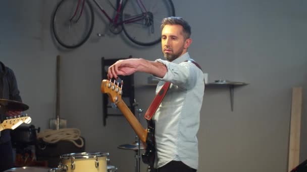 Гітарист налаштовує гітару перед репетицією гурту в гаражі — стокове відео