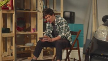 İşten sonra garajdaki adam telefonda oynuyor.