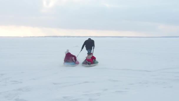 Pappa rullar barn på en slang på is. Långskott — Stockvideo