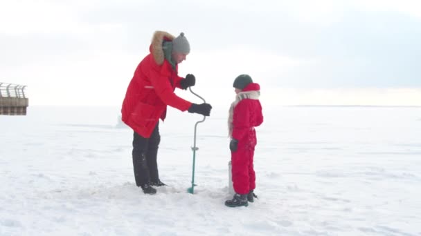 Papa perce un trou pour la pêche et parle avec son fils — Video