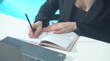 Kadın bir not yazıyor ve dizüstü bilgisayar kullanıyor. Yakın plan.
