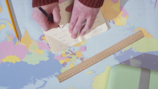 Aventurero escribe en un cuaderno sobre una mesa con un mapa — Vídeo de stock