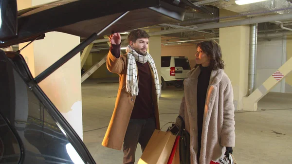 Bir adam çantalı bir kadına arabanın bagajını kapatmasında yardım eder.