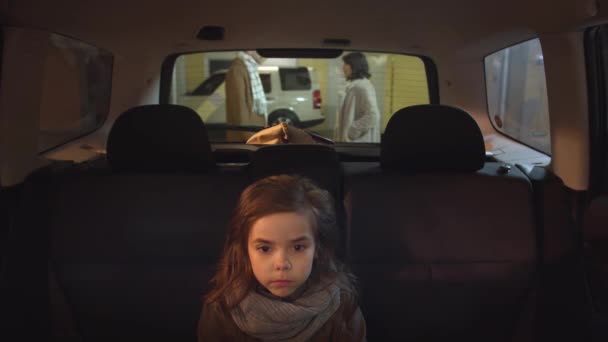 女の子が車の中に座っている。両親は背景で主張する — ストック動画