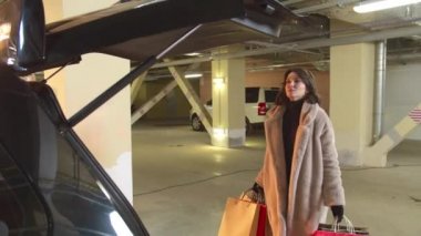 Bir adam çantalı bir kadına arabanın bagajını kapatmasında yardım eder.