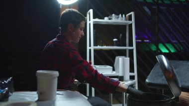 Kadın dövme makinesini temizliyor ve çöp atıyor.