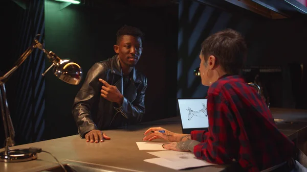 Zenci adam bir dövme sanatçısıyla konuşuyor. Omzuna dövme yaptırmak istiyor.