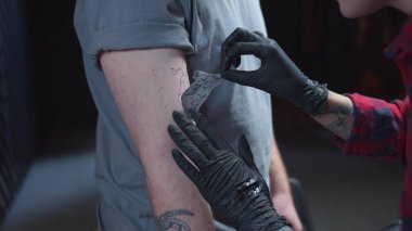 Dövme ustası bir adamın eline bir çizim yapıştırıyor.