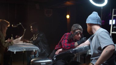 Dövme salonu. İşyerinde usta, müşteriler çizimleri seçer