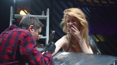 Kız konuşuyor ve acı içinde kıvranırken dövme yaptırıyor.