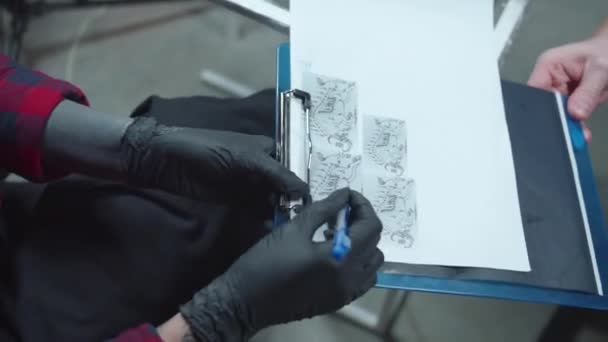 Tattoo Master muestra los bocetos del cliente. Deslizamiento — Vídeos de Stock