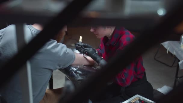 Tatoeëerder zet een tatoeage op een arm van een man. Achtergrond — Stockvideo