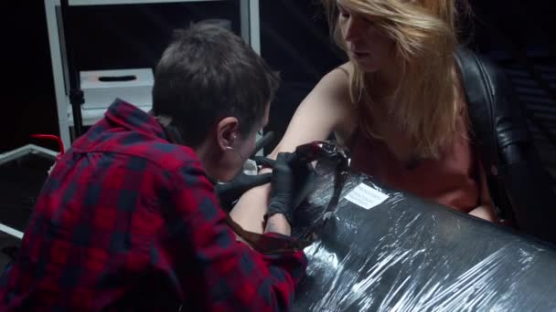Το κορίτσι κάνει τατουάζ στο χέρι ενός πελάτη. Μιλάνε. — Αρχείο Βίντεο
