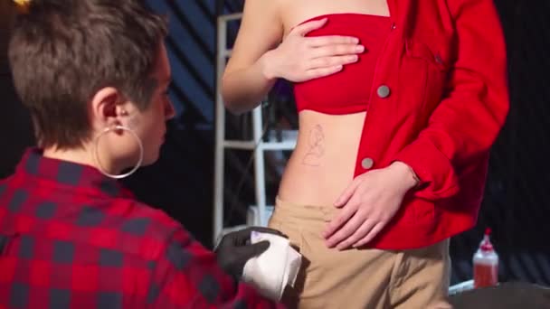 Tatuagem mestre limpa a barriga de uma mulher com uma tatuagem — Vídeo de Stock