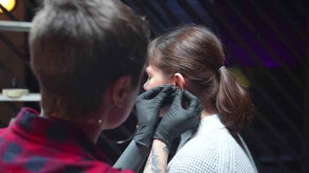 En kosmetolog genomborrar en kvinnas öra med en nål — Stockvideo