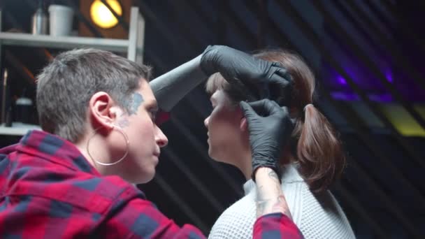 Красавчик вставляет медицинскую сережку в ухо девушки — стоковое видео