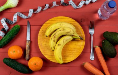 Tahta tabakta muz, avokado, portakal, havuç, soğan, salatalık ve kırmızı ahşap bir masada bir şişe su.