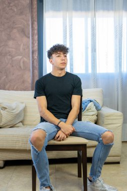 Genç adam oturma odasında beyaz bir kanepede poz veriyor.