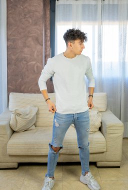 Genç adam oturma odasında beyaz bir kanepede poz veriyor.