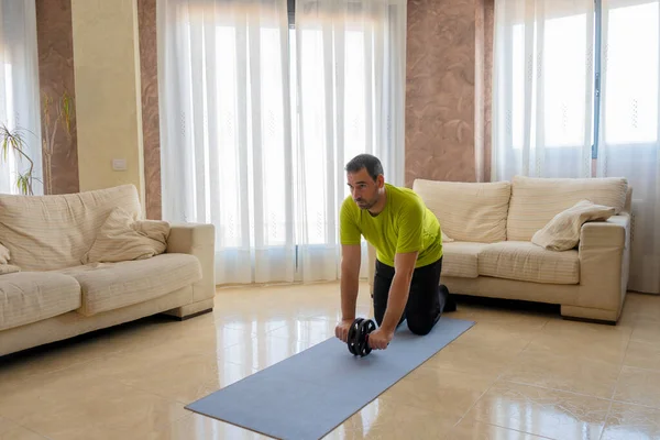 畳の上のソファの前に彼のリビングルームで黒と緑のスポーツウェアで運動する低形状の髭の男 — ストック写真