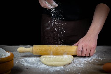 Adam elleri siyah arka planı olan ahşap bir masada ekmek hamuru yoğuruyor. Sanatsal kavram