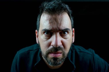 Siyah kazak giymiş sakallı bir adamın portresi zorlu bir tavırda siyah bir arkaplanda. Yalnızlık kavramı.